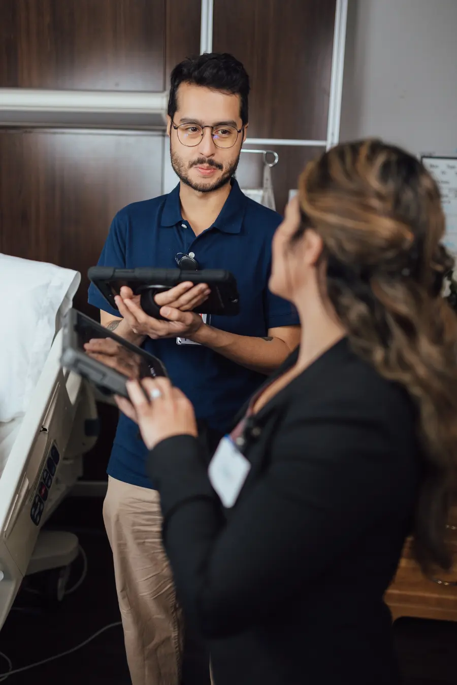 Man wearing glasses holds electronic tablet while talking to woman in office