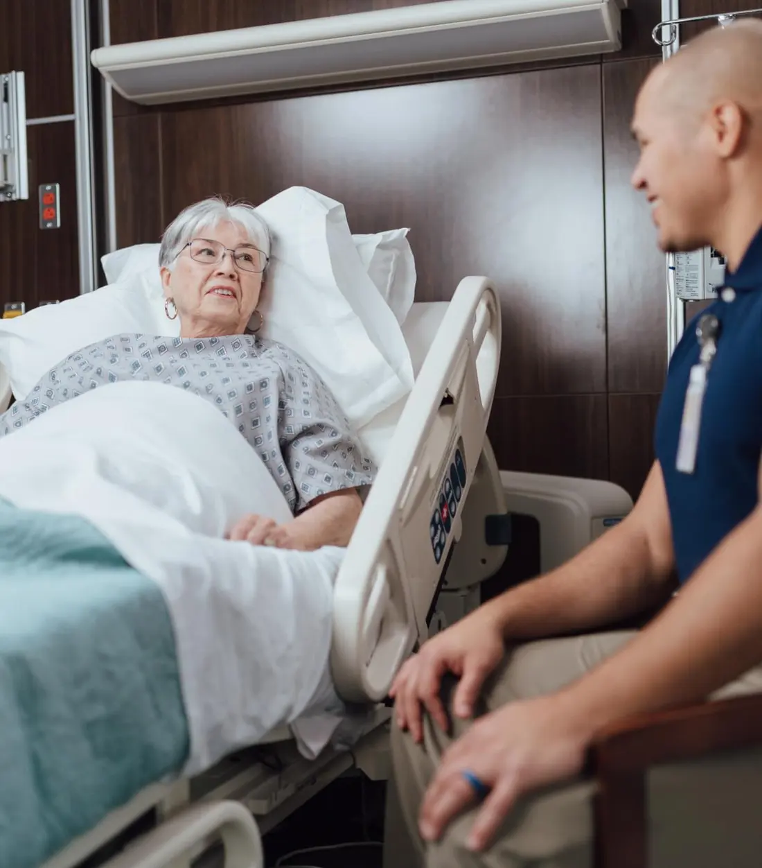 Elderly patient in a hospital bed talking with a healthcare worker
