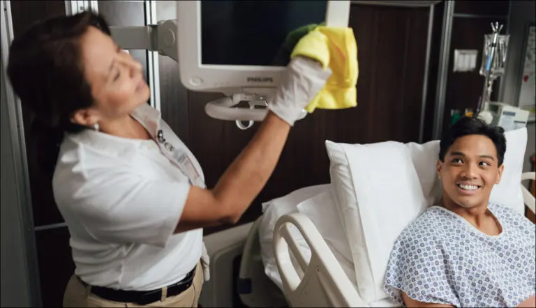 Environmental services associate cleaning a hospital room while the patient smiles